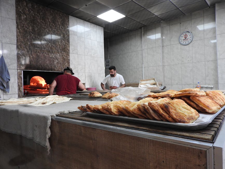 Two bakers preparing bread in a traditional wood-fired oven bakery with visible fresh pastries.